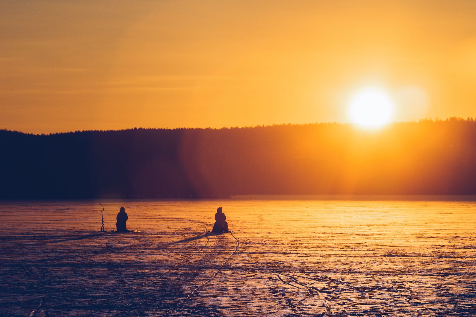 Pêche blanche au coucher du soleil sur le lac gelé